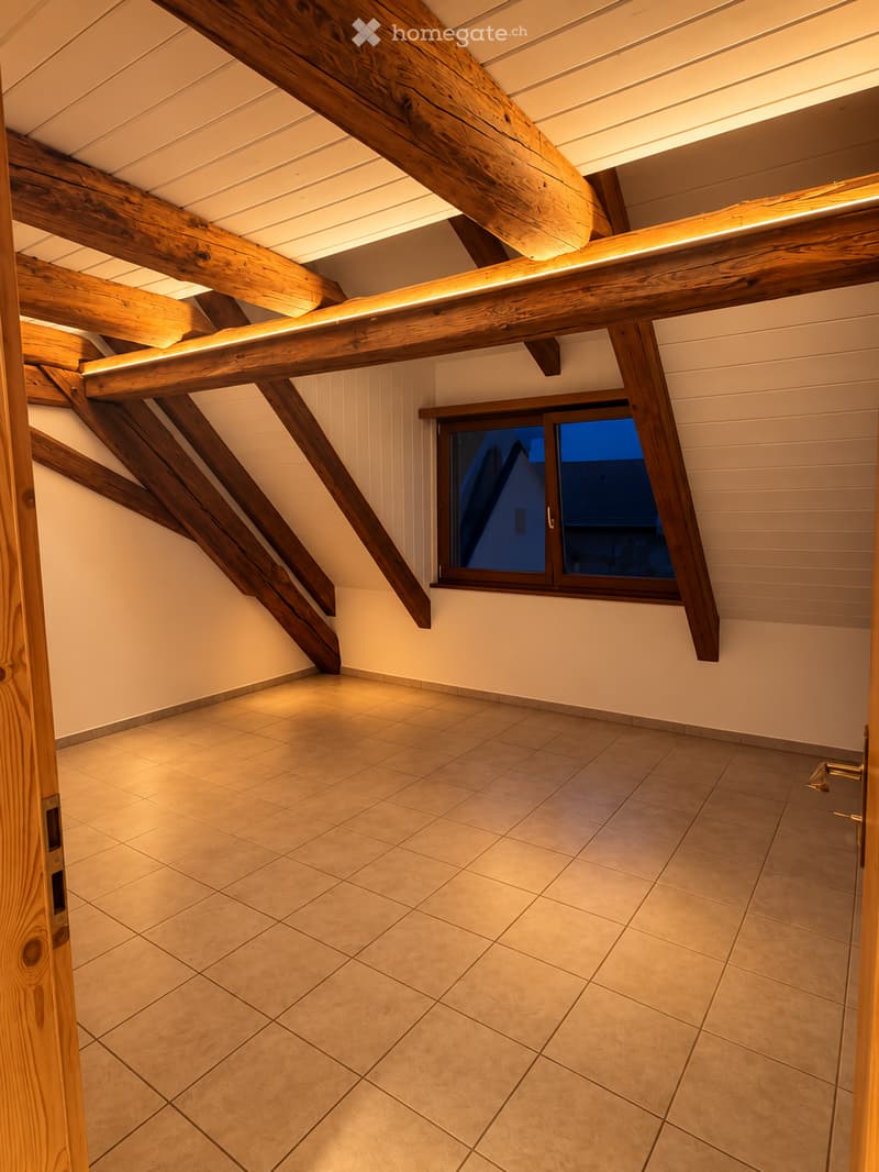 Empty room with exposed wooden beams, tiled floor, and a single window showing a dark exterior view.