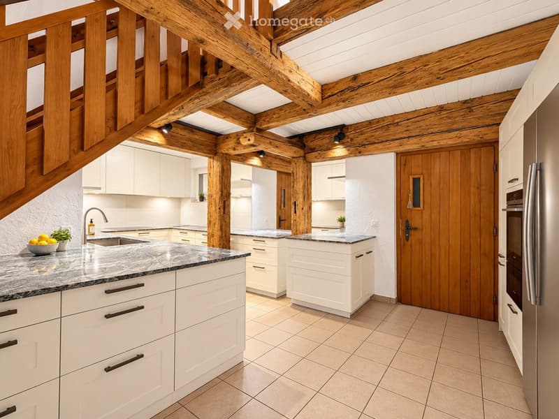 Modern kitchen with white cabinets, marble countertops, stainless steel appliances, and exposed wooden beams on the ceiling.