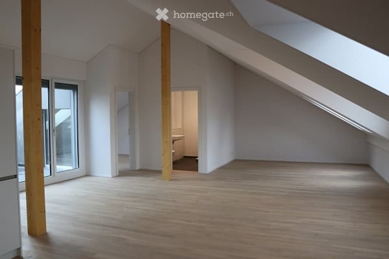 Bright, empty attic room with wooden flooring, white walls, and large windows. No furniture or equipment present.