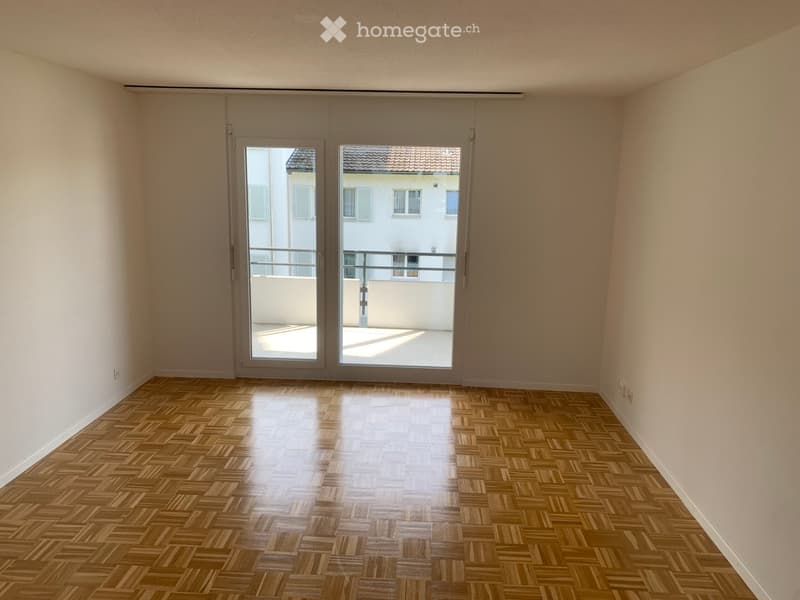 Empty room with wooden herringbone flooring, large sliding glass doors leading to a balcony, and light-colored walls.