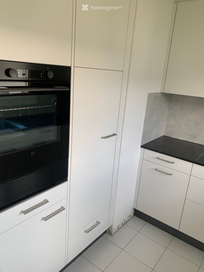 Modern kitchen with white cabinets, stainless steel handles, and a built-in oven. The countertops are black, and the floor is tiled.