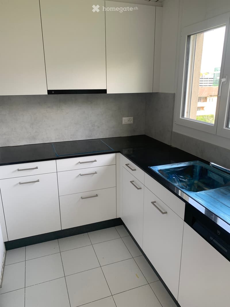 Modern kitchen with white cabinets, black countertops, and a built-in oven. Features a sink with a faucet and a window overlooking the outside.