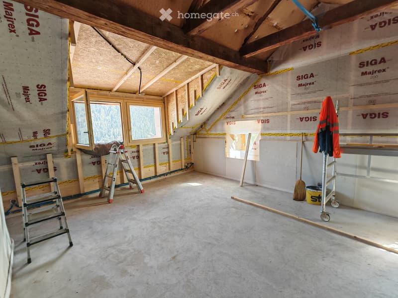 Empty attic space with exposed wooden beams, insulation, and construction materials. Features include a window, ladders, and a broom.