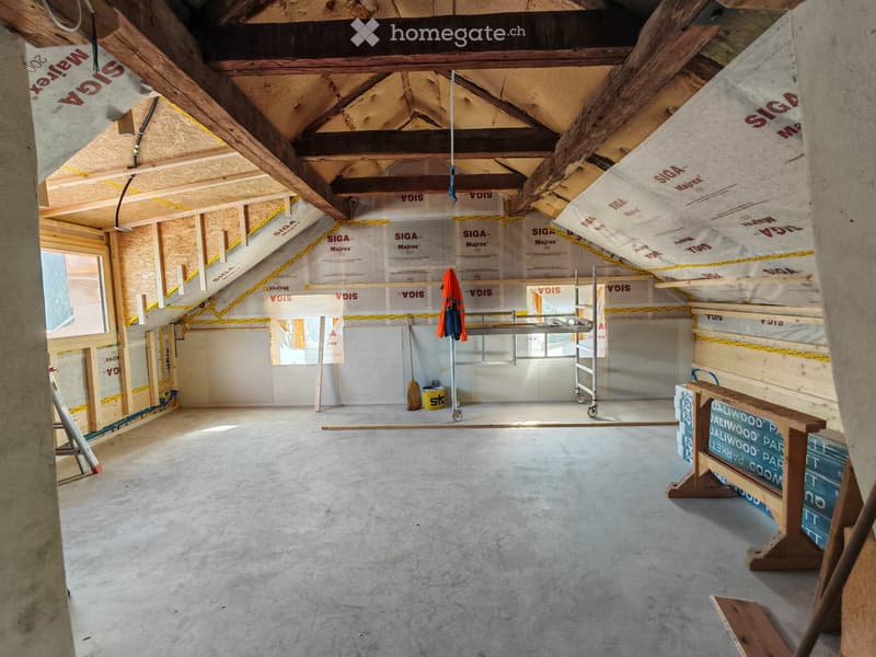 Empty attic space with exposed wooden beams, insulation, and construction materials. No furniture or furnishings present.