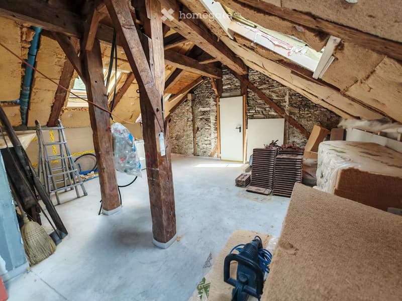 Empty attic space with exposed wooden beams, stone walls, and construction materials scattered around.