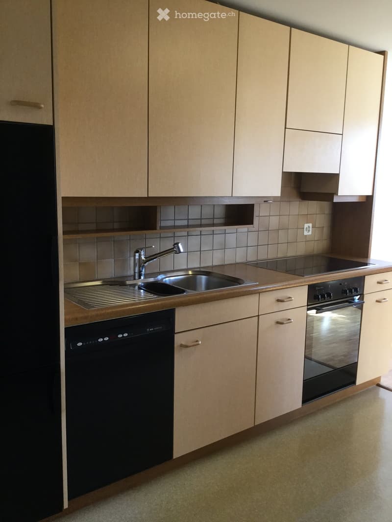 Modern kitchen with light wood cabinets, stainless steel sink, faucet, oven, and dishwasher.