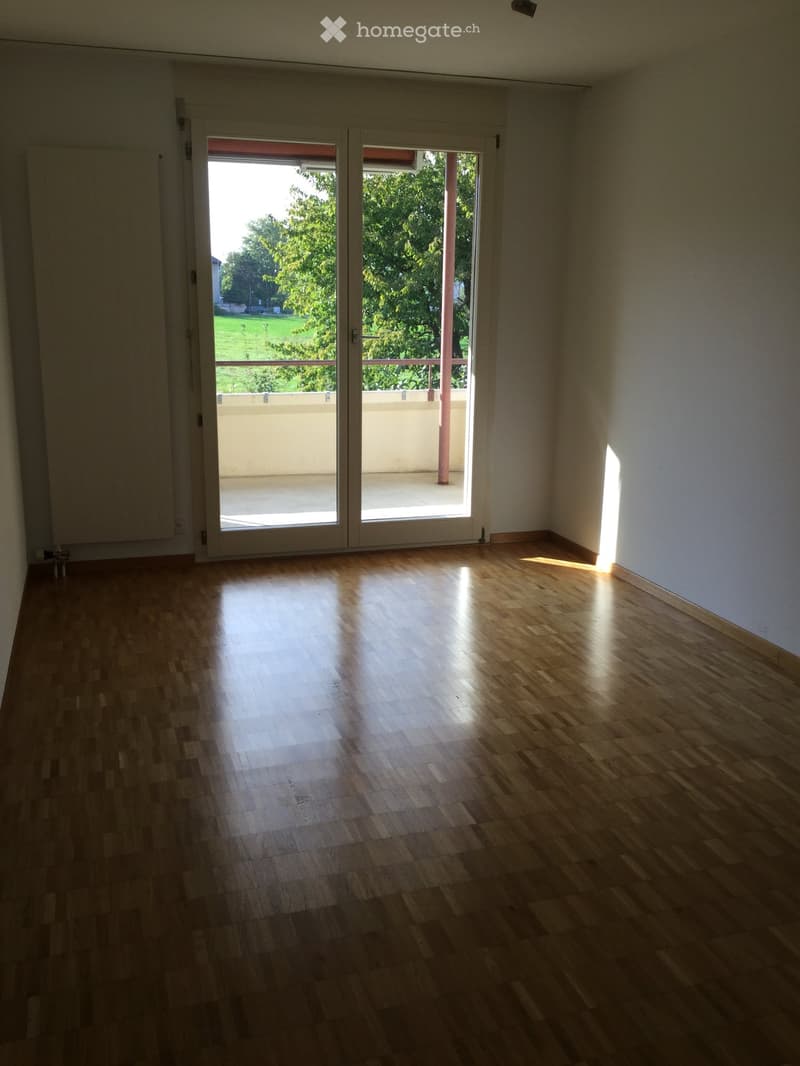 Empty room with wooden flooring and large sliding glass doors leading to a balcony with outdoor view.