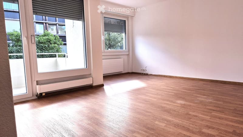Empty room with wooden flooring, large windows, radiators, and natural light. No furniture or equipment present.