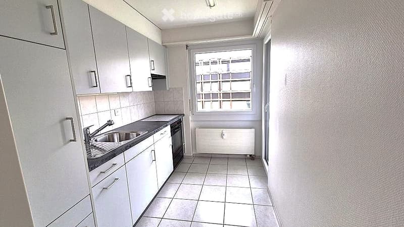 Modern kitchen with white cabinets, tiled floor, stainless steel sink, and built-in oven.