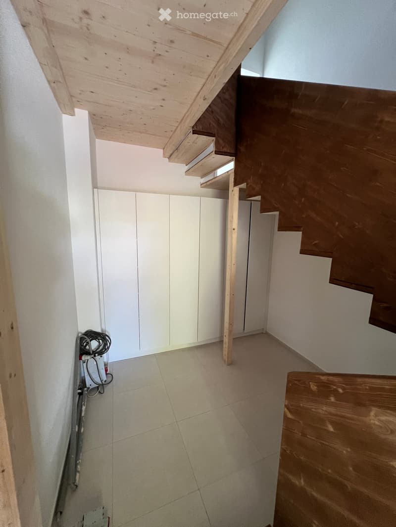 Empty hallway with tiled floor, white walls, wooden staircase, and built-in white cabinets.