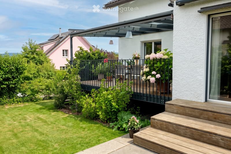 Well-maintained garden with green lawn, wooden steps leading to a covered patio area, potted plants, and a black metal railing.