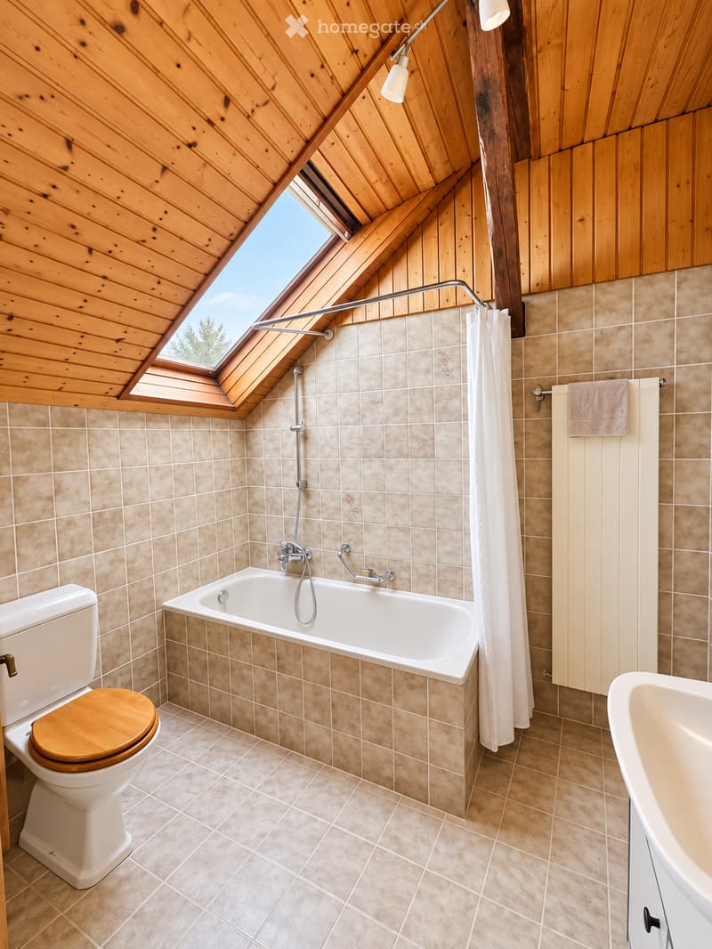 Bathroom with wooden ceiling, skylight window, beige tiled walls, bathtub, toilet with wooden seat, shower area, and radiator with towel.