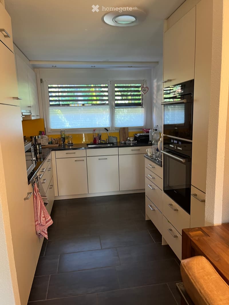 Modern kitchen with white cabinets, dark tiled floor, and stainless steel appliances including an oven and sink.