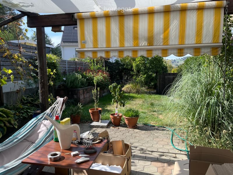 Garden area with a covered patio, hammock, potted plants, and a wooden table with various items on it.