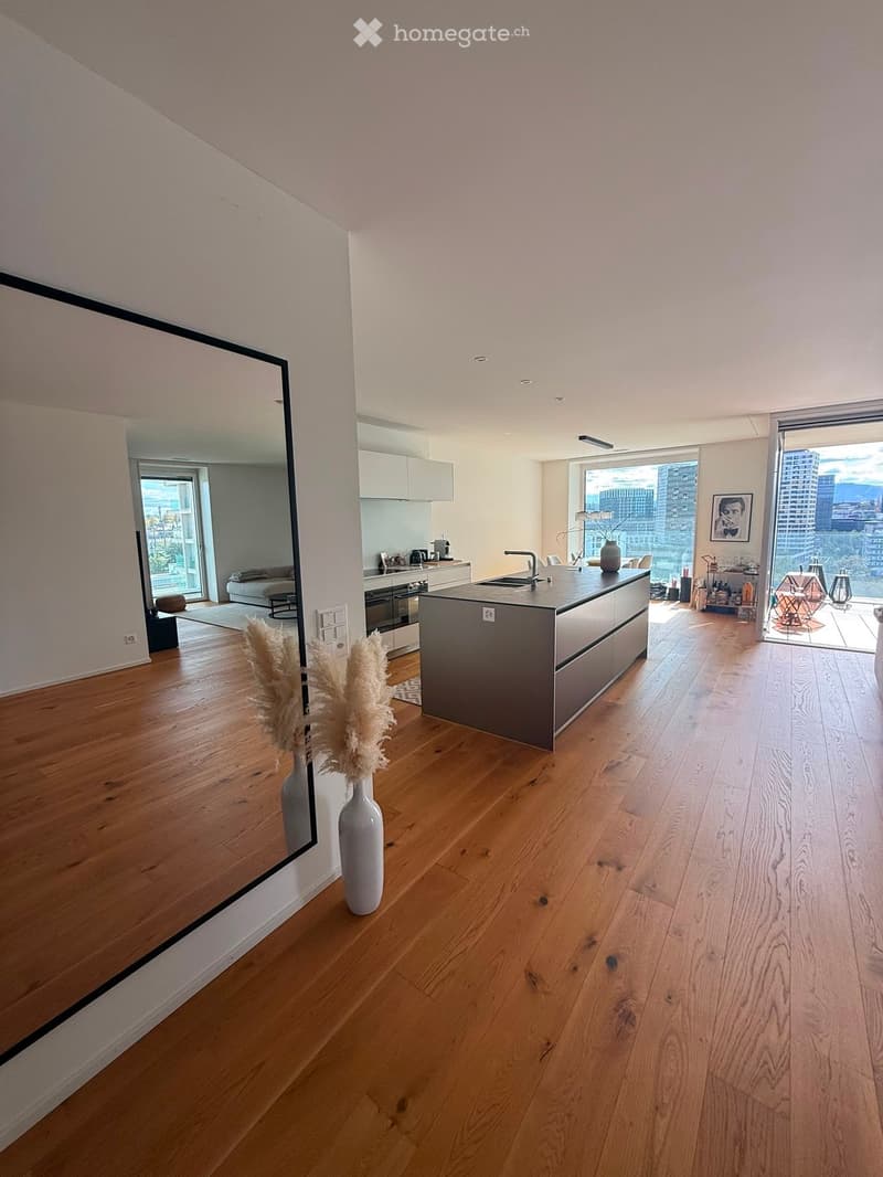 Open-concept kitchen and living area with wooden flooring, modern kitchen island, large windows offering city views, and decorative vases.