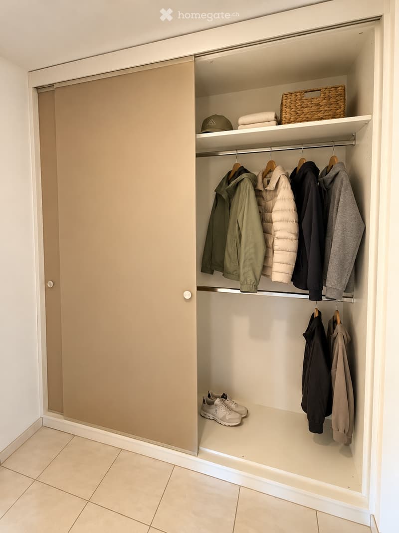 Empty closet with built-in shelving and hanging space, featuring a sliding door and tiled floor.