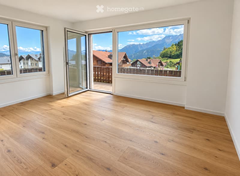 Empty room with light wooden flooring, white walls, large windows, and sliding glass doors opening to a balcony with a scenic mountain view.