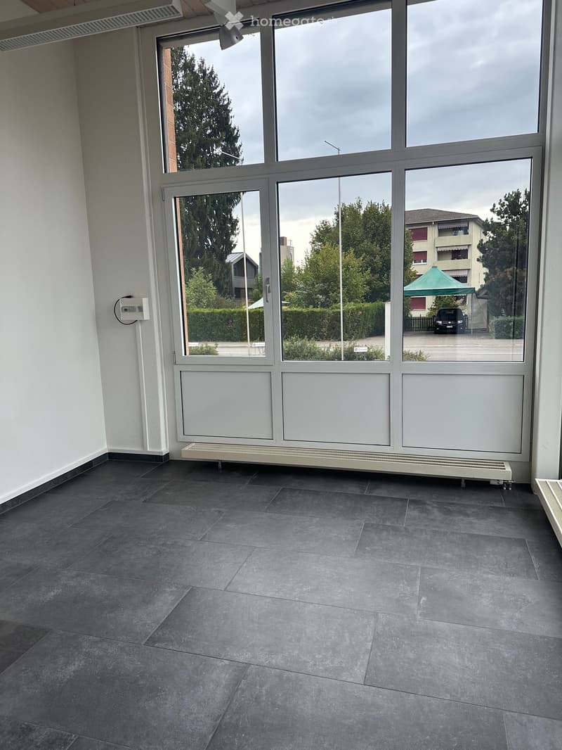 Empty room with large windows, grey tiled floor, white walls, radiator, and electrical outlet.