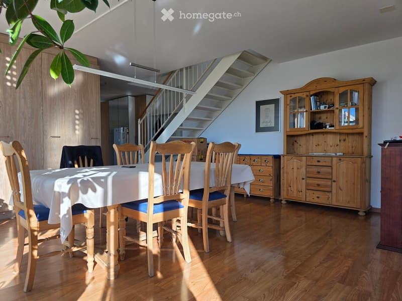 Bright dining area with wooden floor, dining table with chairs, wooden cabinet, and staircase leading to another level.