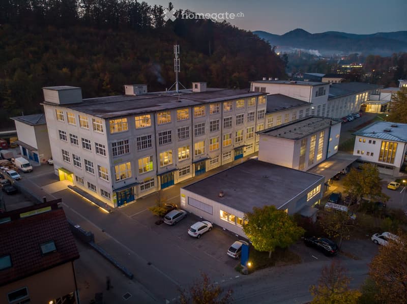 Aerial view of a large multi-building complex with illuminated windows, surrounded by parked cars and trees.