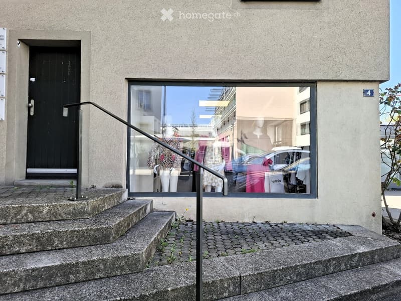 Concrete stairs leading to a door with metal handrail, storefront window with clothing display