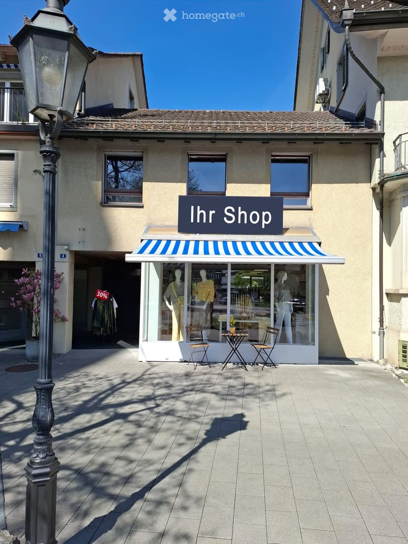 a shop with blue and white awning, a large window on display and outdoor chairs