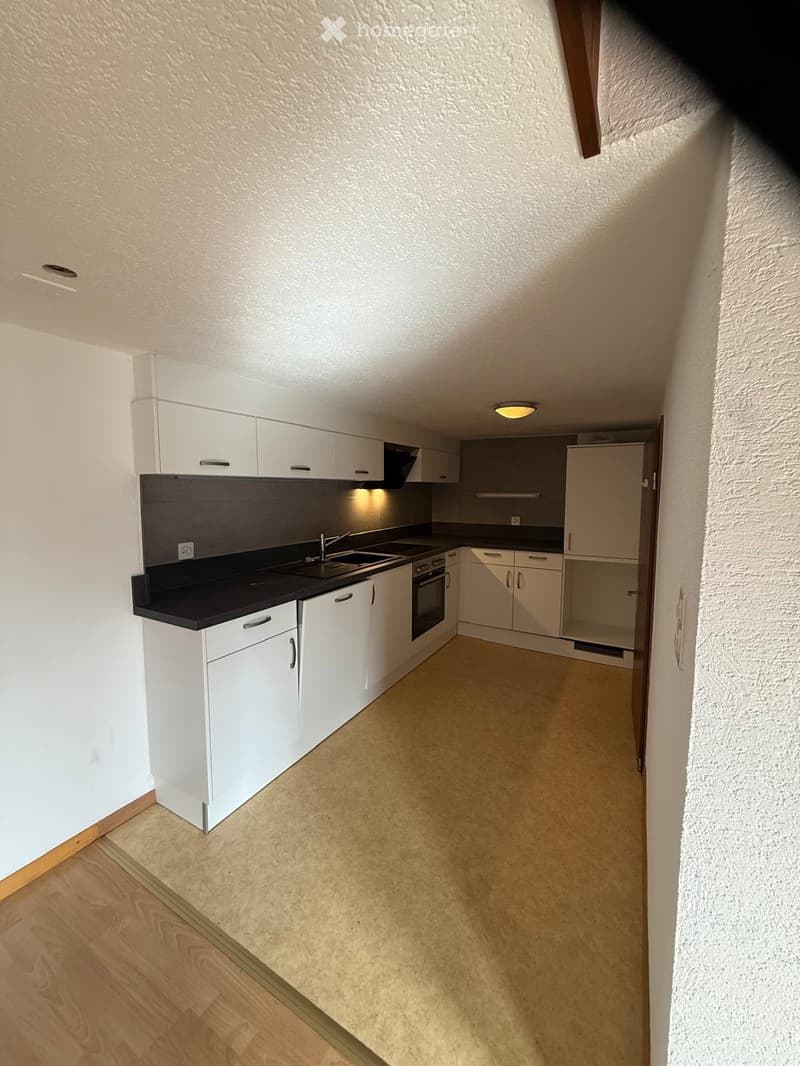 Modern kitchen with white cabinets, black countertop, sink, and oven. The space features a mix of wooden and tiled flooring.