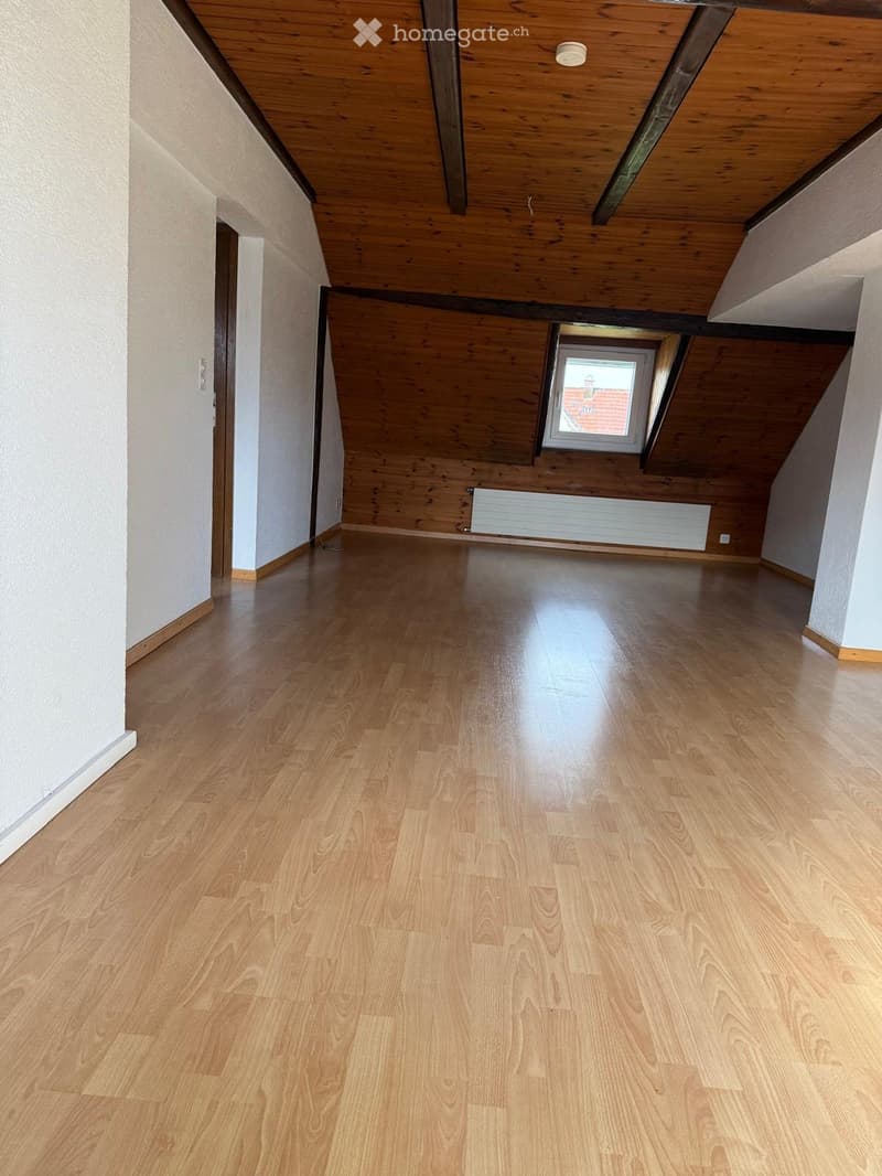 Empty attic space with wooden flooring, exposed wooden beams, and a skylight window. No furniture or equipment present.