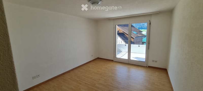 Empty room with wooden flooring and white walls, featuring a large sliding glass door leading to a balcony or outdoor area.