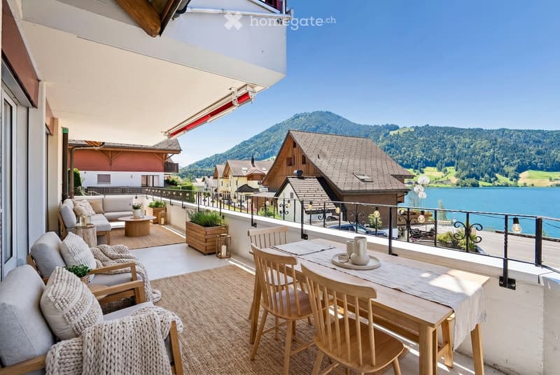 Balcony with a scenic mountain and lake view, furnished with a sofa, chairs, a dining table, and decorative items.