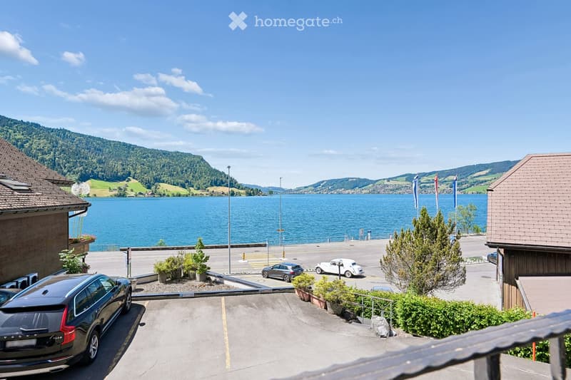 View from a balcony overlooking a parking area, lake, and surrounding hills with flags and parked cars.