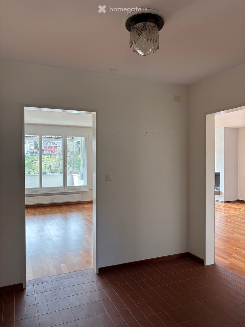Empty room with wooden flooring, large window with view, and a chandelier light fixture.