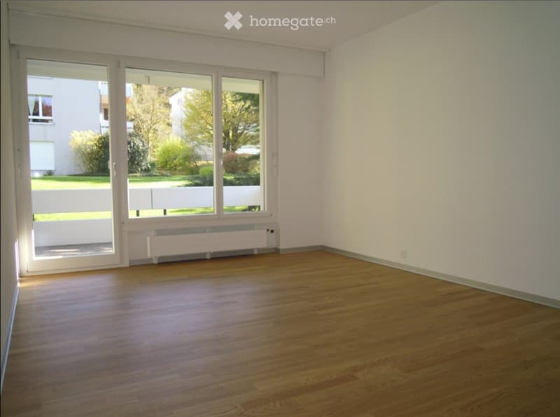 Empty room with wooden flooring, large windows, and white walls. No furniture or equipment present.
