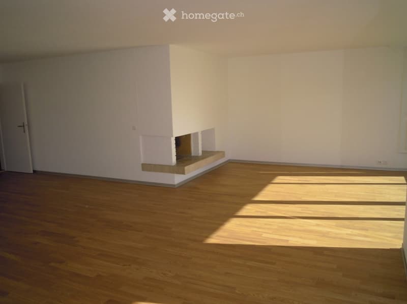 Empty room with light wooden flooring and white walls, featuring a small built-in shelf unit and a door on the left side.