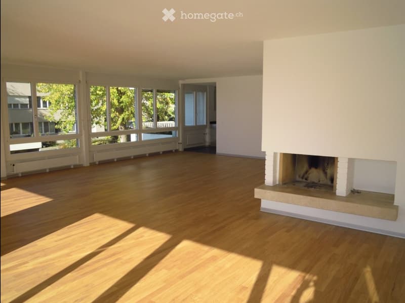 Empty room with wooden flooring, large windows, and a fireplace with a white surround.