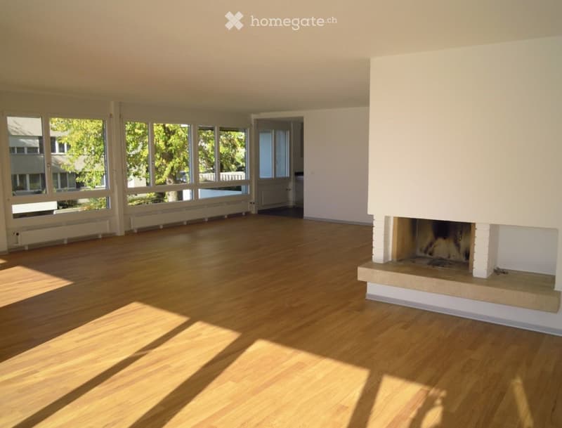 Empty room with wooden flooring, large windows, and a fireplace.