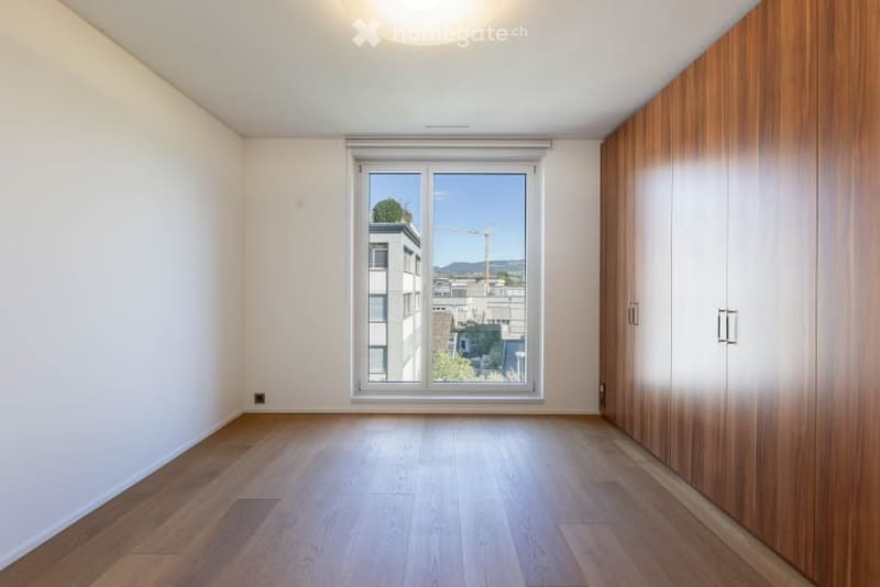 Empty room with wooden flooring, white walls, large window with view, and built-in wooden closet.