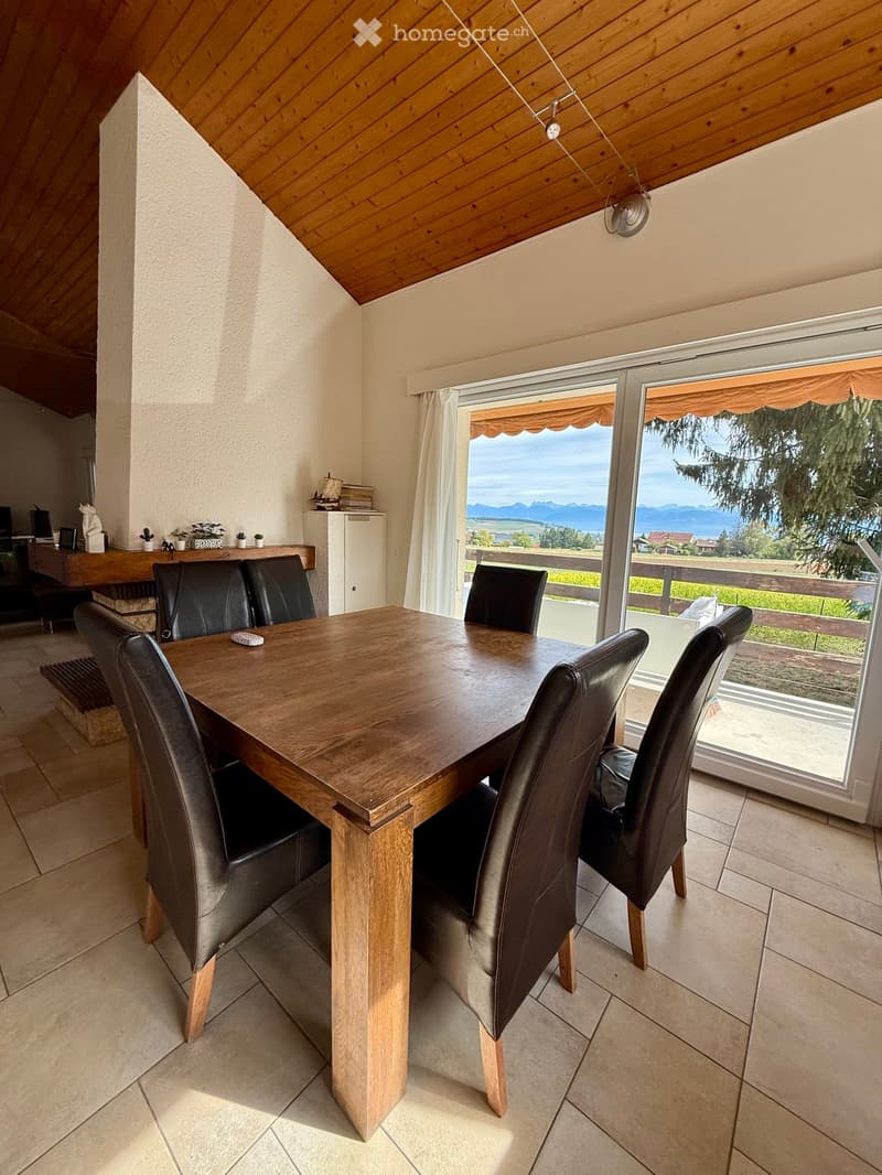 Dining room with a wooden table, six black leather chairs, a cabinet, and a large window offering a scenic view of mountains and greenery.