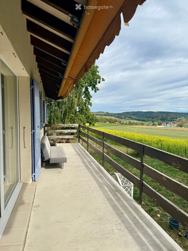 Balcony with wooden railing, bench, and scenic countryside view.