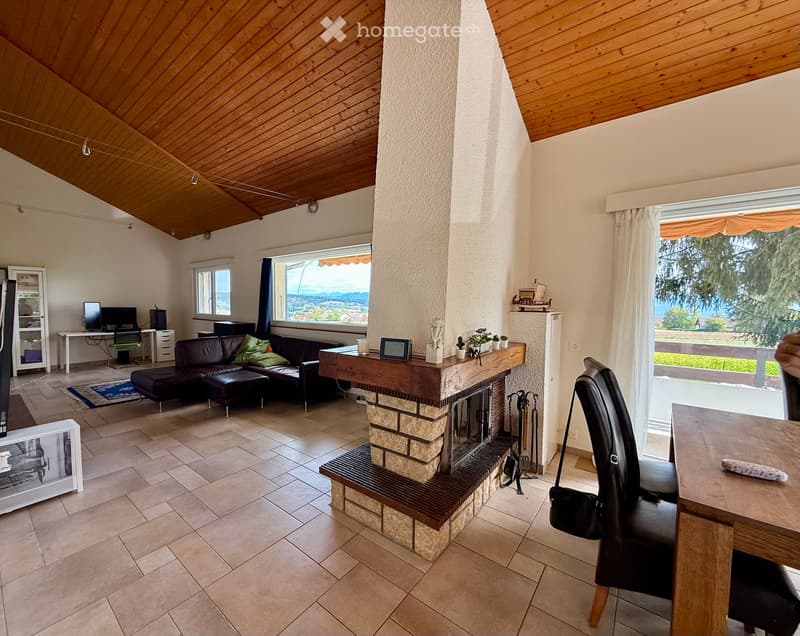 Living room with a fireplace, large windows offering a scenic view, a sofa, coffee table, and a chair near the window.