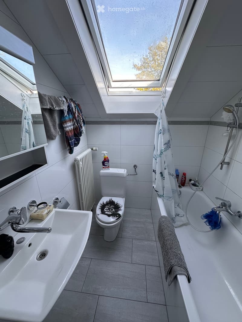 Modern bathroom with white tiles, a sink, toilet, bathtub, radiator, and large skylight windows.