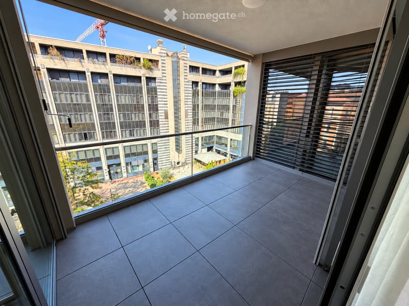 Modern balcony with tiled floor, large windows, metal railing, and a view of a contemporary building complex with greenery.