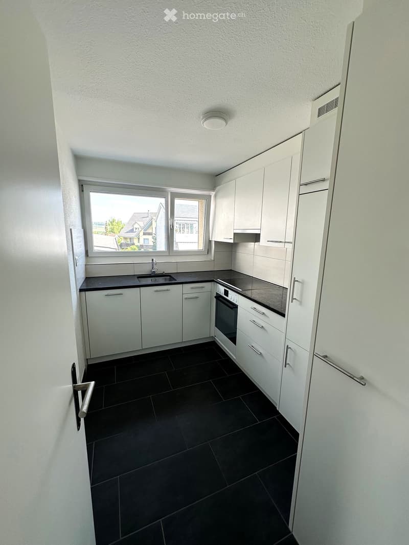 Modern kitchen with white cabinets, black countertops, and black tiled floor. Features a sink, faucet, and oven.