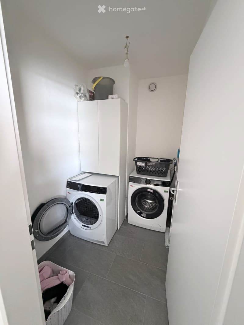 Compact bathroom with a washing machine, dryer, and cabinet. Laundry basket and additional items are visible.
