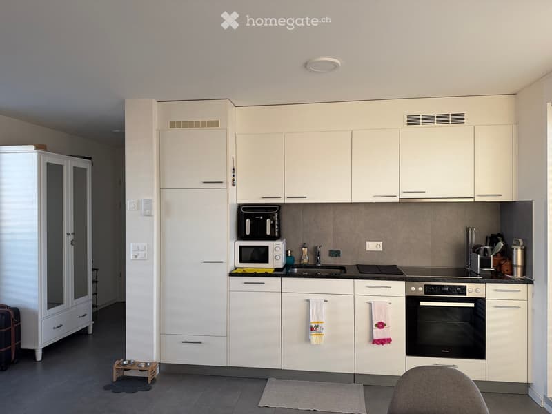 Modern kitchen with white cabinets, stainless steel appliances, and a black countertop. Includes a refrigerator, oven, microwave, toaster, sink, and various kitchen items.