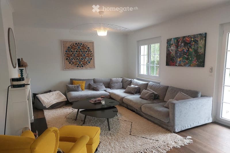 Modern living room with a grey sectional sofa, yellow accent chair, black coffee table, and large windows allowing natural light. Features include a white shag rug, decorative art pieces, and a sleek floor lamp.