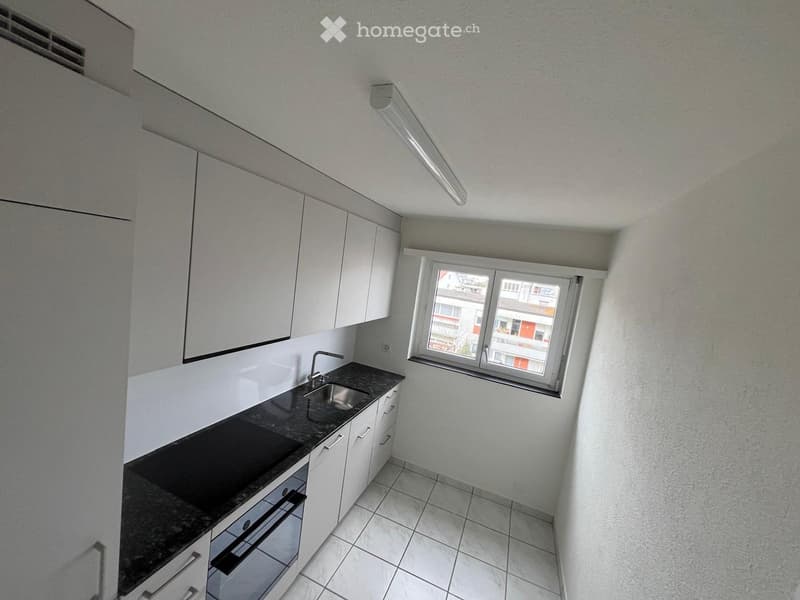 Modern kitchen with white cabinets, dark countertop, sink, and a window overlooking a building exterior.