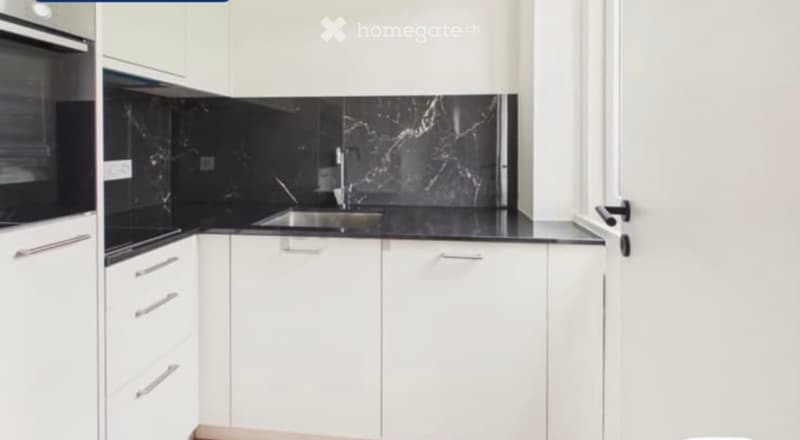 Modern kitchen with white cabinets, black marble backsplash, and stainless steel sink.