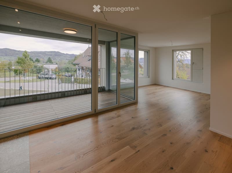 Empty room with wooden flooring, large sliding glass doors leading to a balcony, and white walls.