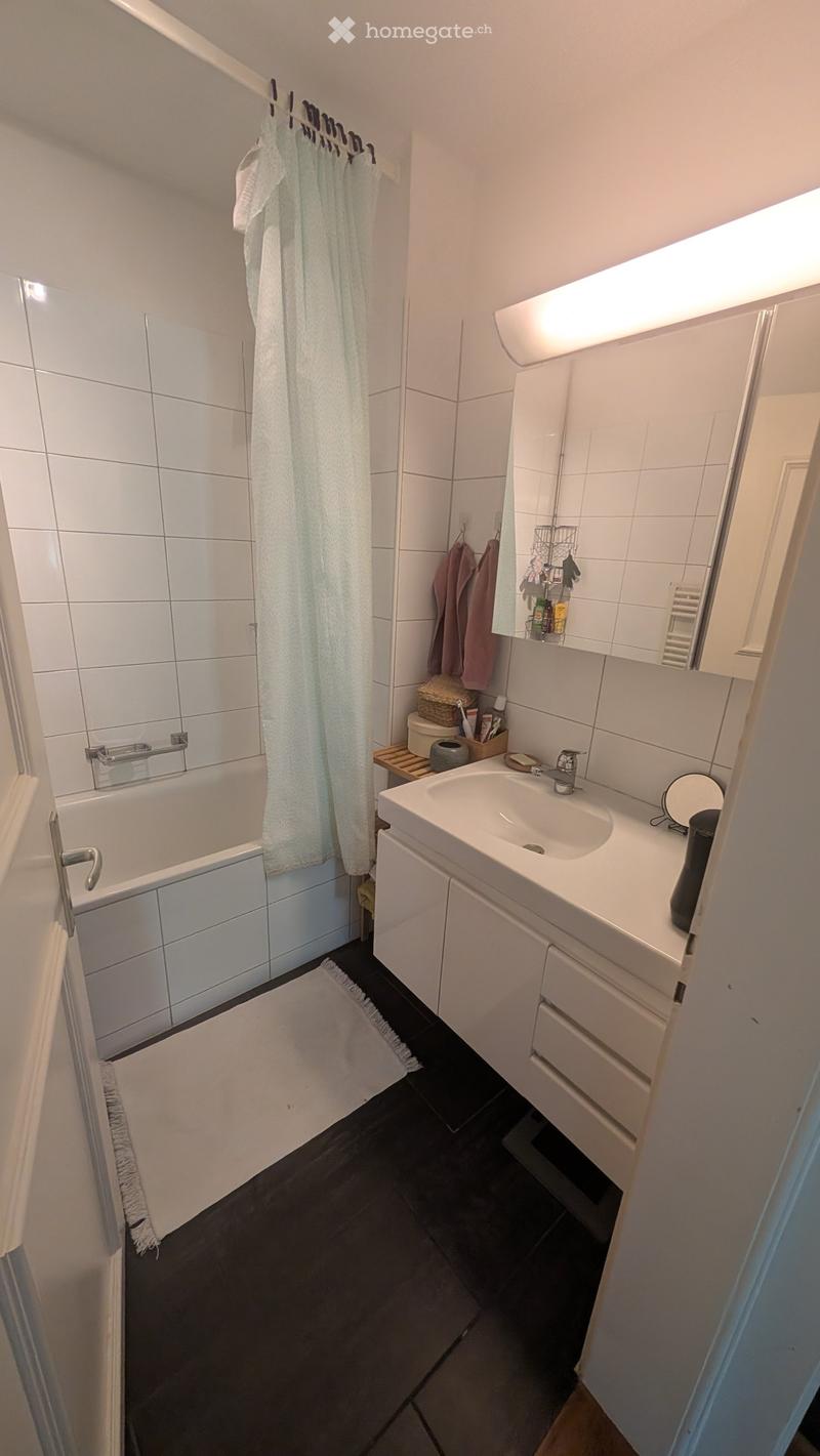 Modern bathroom with white tiles, a bathtub, a sink with a mirror, and a shower area with a curtain.
